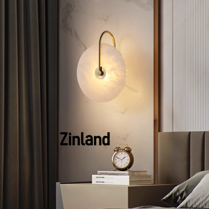 Elegant gold alabaster wall lamp with a curved brass arm, mounted beside a modern bed for warm ambient lighting.